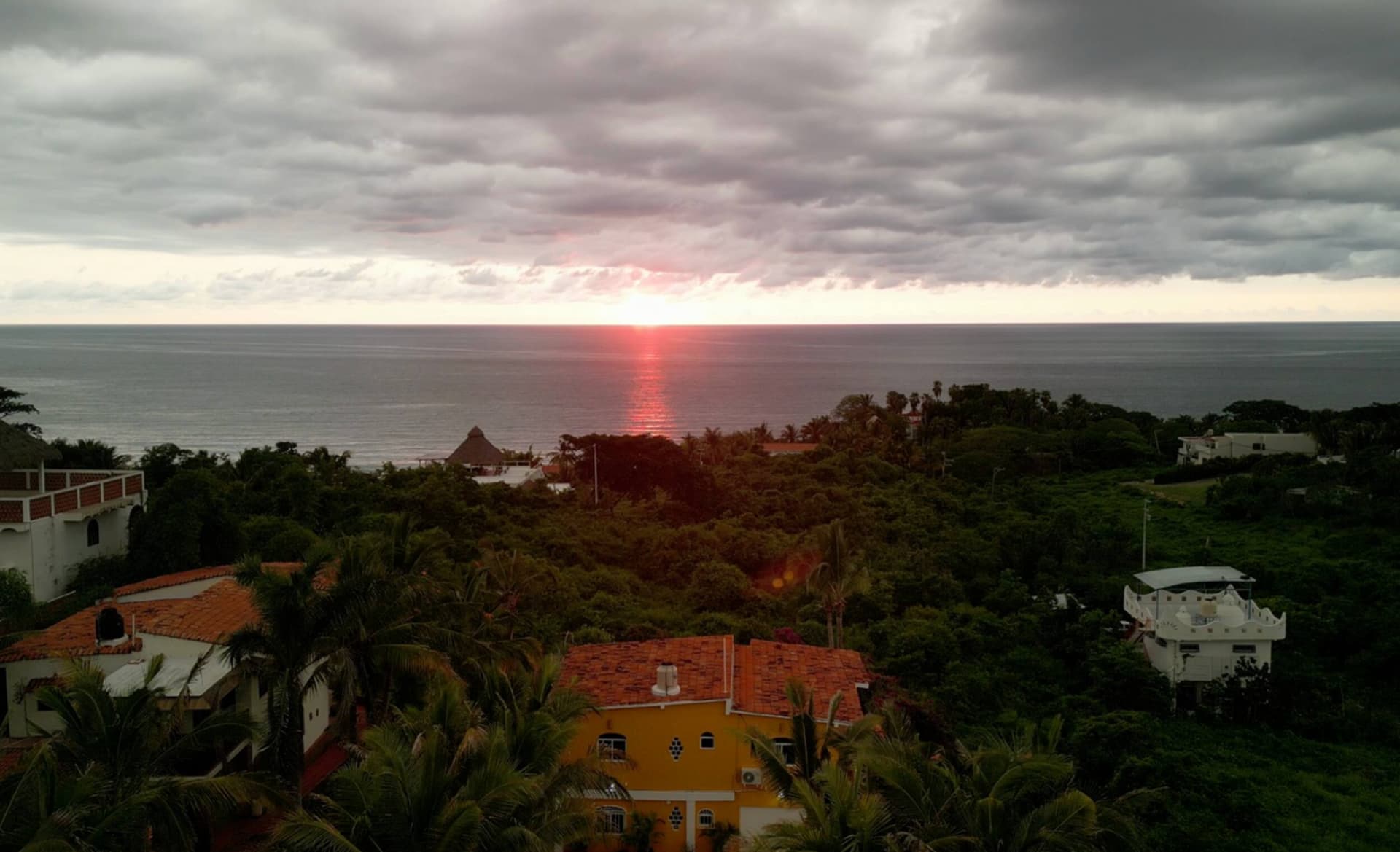 Aerial view of Casa de Mango and the surrounding hilltop neighbourhood at sunset, with the Pacific Ocean on the horizon