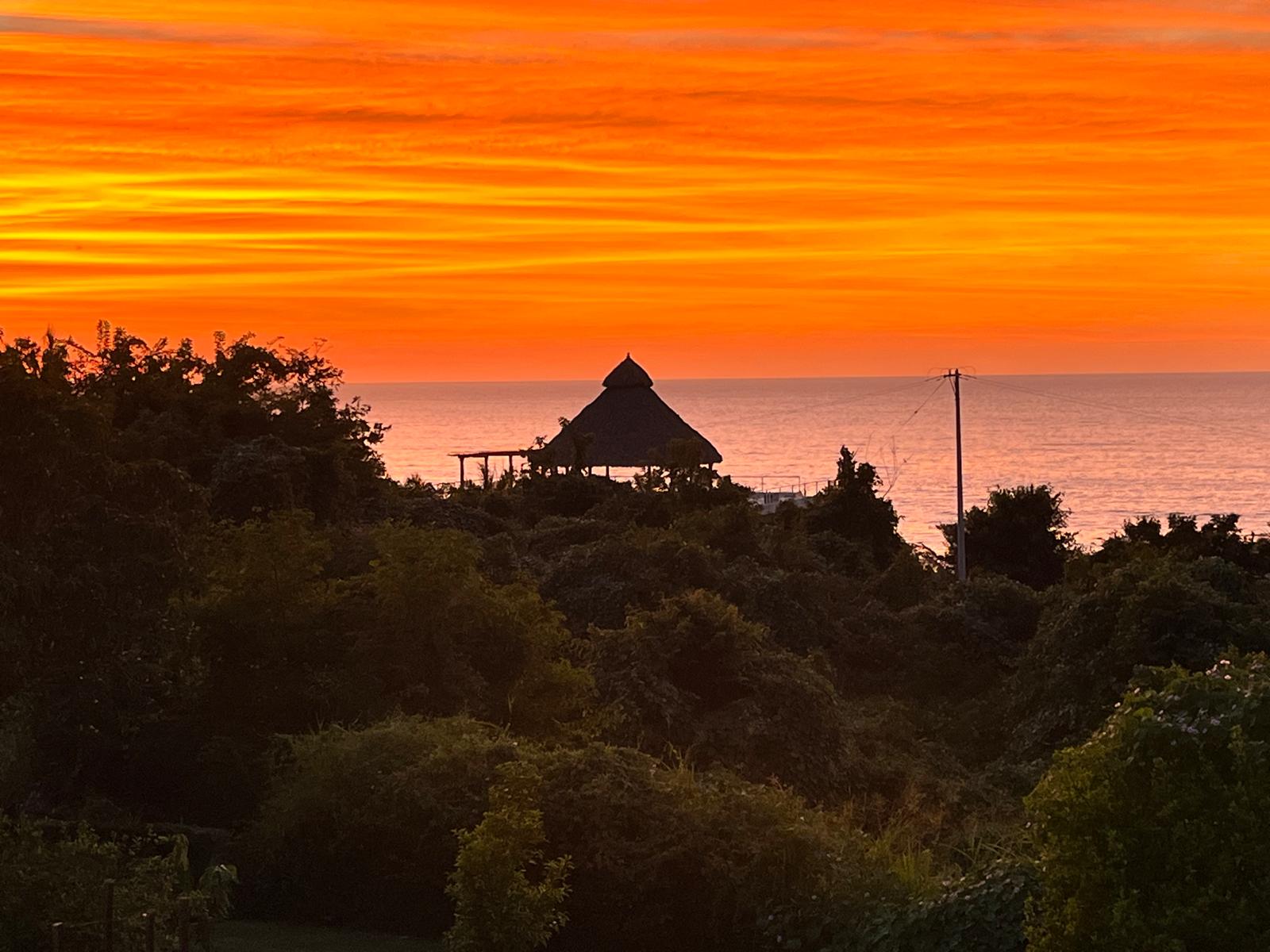 Casa de Mango's thatched hilltop palapa silhouetted against a burning orange sunset over the Pacific