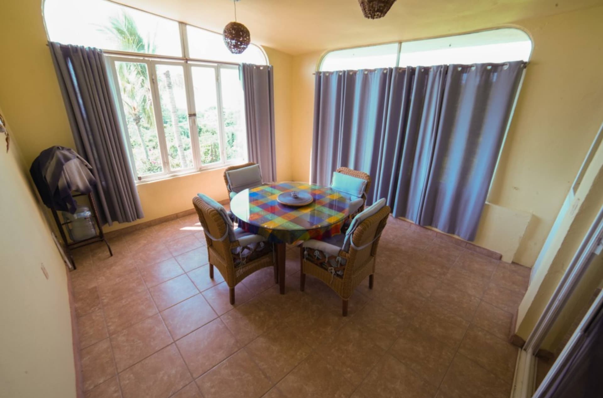 Bright indoor dining terrace with a colourful tiled table, wicker chairs and tall windows looking out to palm trees